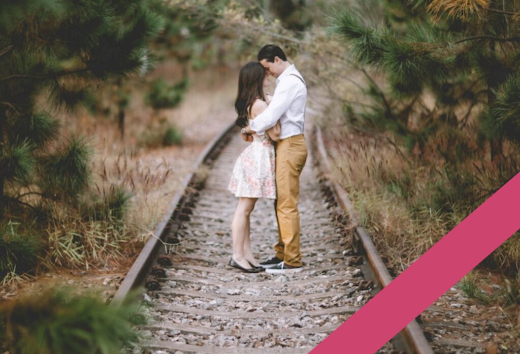 couple standing on rail road tracks while kissing