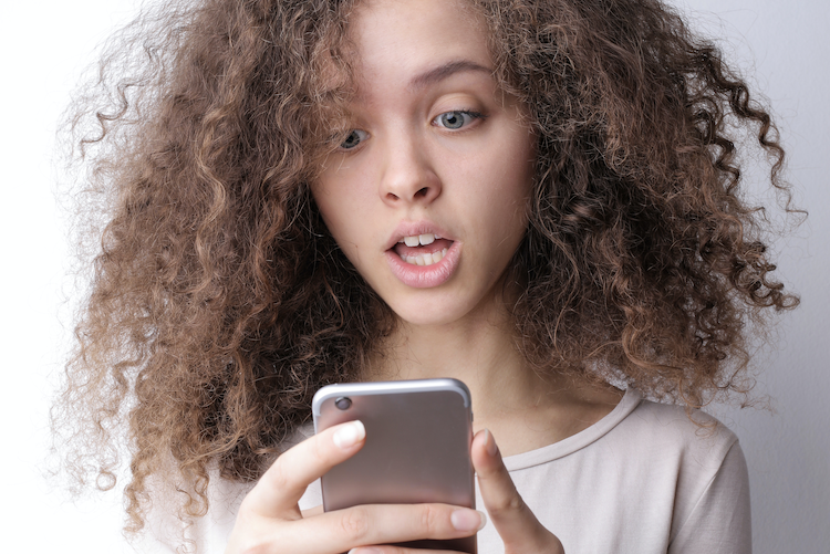 young woman looking at phone with a shocked look on face