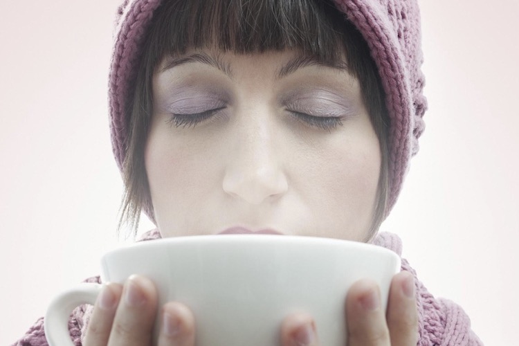 young woman drinking a warm drink in a big white mug