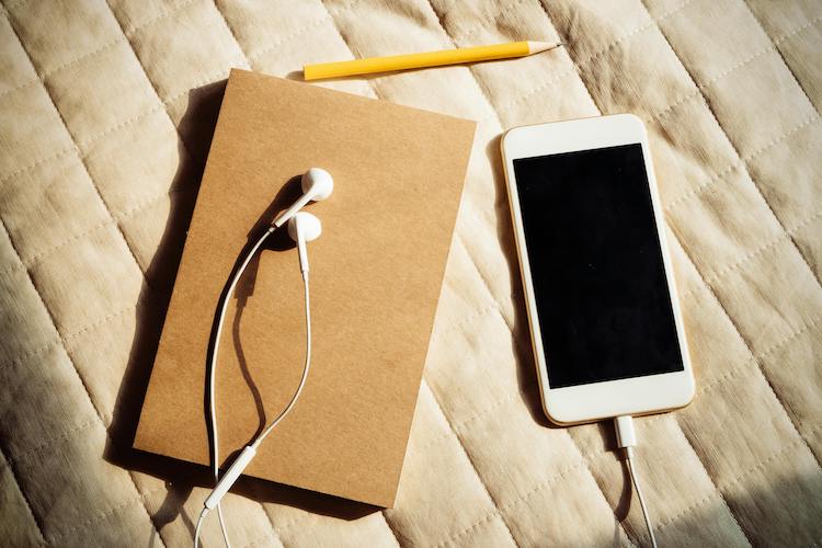 journal, earbuds and phone on a bed
