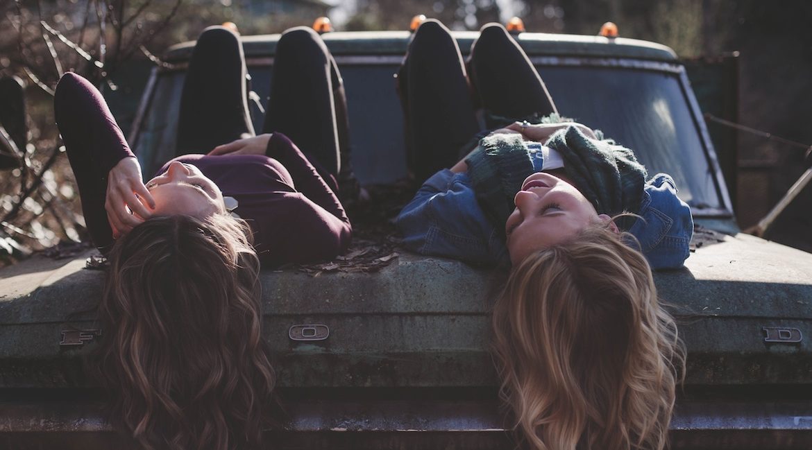 girls laying on the back of an old beat up car